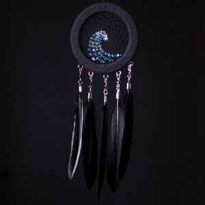 May include: A black dreamcatcher with a blue and white beaded wave design and black feathers hanging from the bottom.