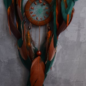 May include: A brown and green dreamcatcher with feathers and beads. The dreamcatcher has a circular design with a web-like pattern in the center.