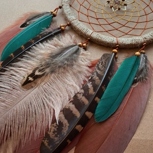 May include: A dream catcher with a brown and white woven net, decorated with brown beads and feathers. The feathers are brown, white, teal, and black.