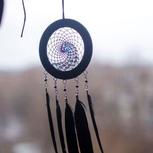 May include: A black dreamcatcher with a purple and blue beaded web and black feathers hanging from it.