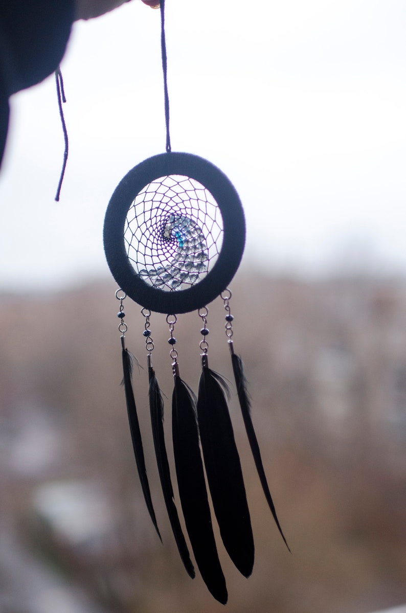 May include: A black dreamcatcher with a purple and blue beaded web and black feathers hanging from it.