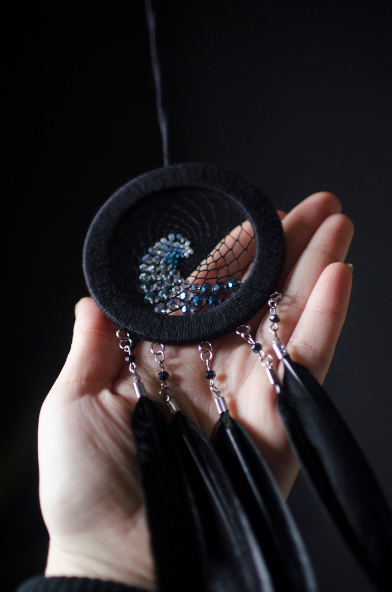 May include: A black dreamcatcher with blue and silver beads and black feathers hanging from it.