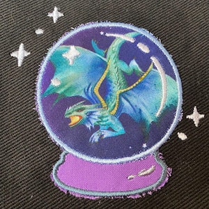 May include: A purple snow globe with a blue dragon inside. The dragon has green wings and is flying in a starry sky.