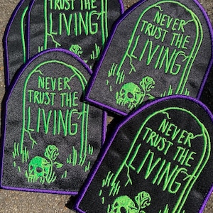 May include: Five black and green embroidered iron-on patches with a tombstone design. Each patch features a skull and rose with the text "Never Trust The Living" in green.