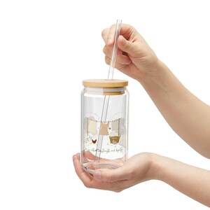 May include: A clear glass tumbler with a wooden lid and a clear straw. The tumbler features a whimsical design of clothes hanging on a clothesline with the text "She is clothed with strength and dignity."