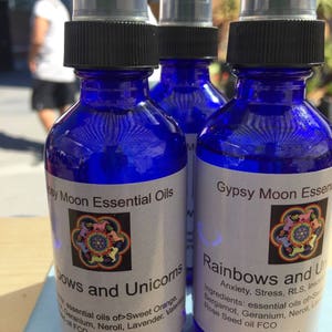 May include: Three blue glass bottles with black spray tops and white labels. The labels feature a rainbow-colored design with the text "Rainbows and Unicorns" and "Gypsy Moon Essential Oils". The bottles are 2 oz each.