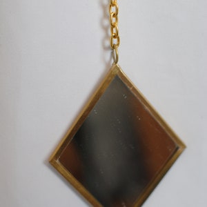 May include: A gold diamond-shaped mirror with a gold chain hanging from the top.