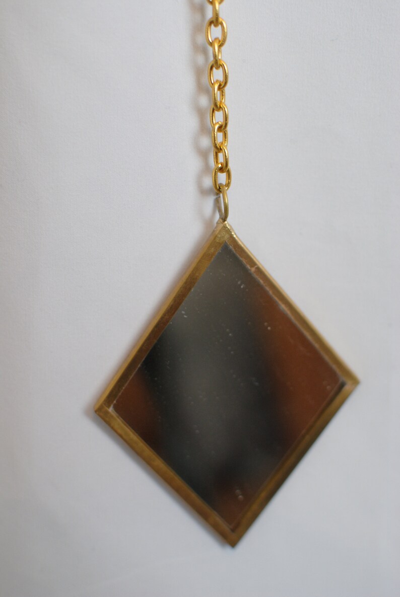May include: A gold diamond-shaped mirror with a gold chain hanging from the top.