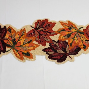 May include: A beaded table runner featuring a design of autumn leaves in shades of red, orange, and yellow.