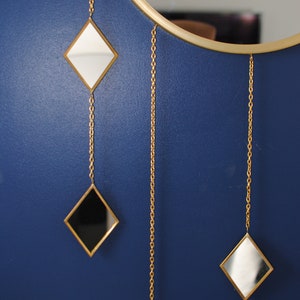 May include: A round mirror with a gold frame and three smaller diamond-shaped mirrors hanging from chains. The smaller mirrors are black, white, and silver.