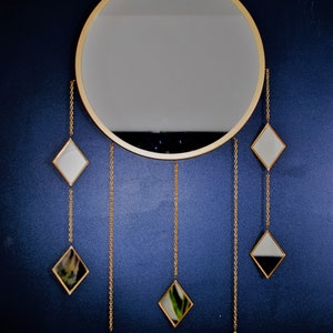 May include: A gold round mirror with a gold frame and six smaller diamond-shaped mirrors hanging from chains.