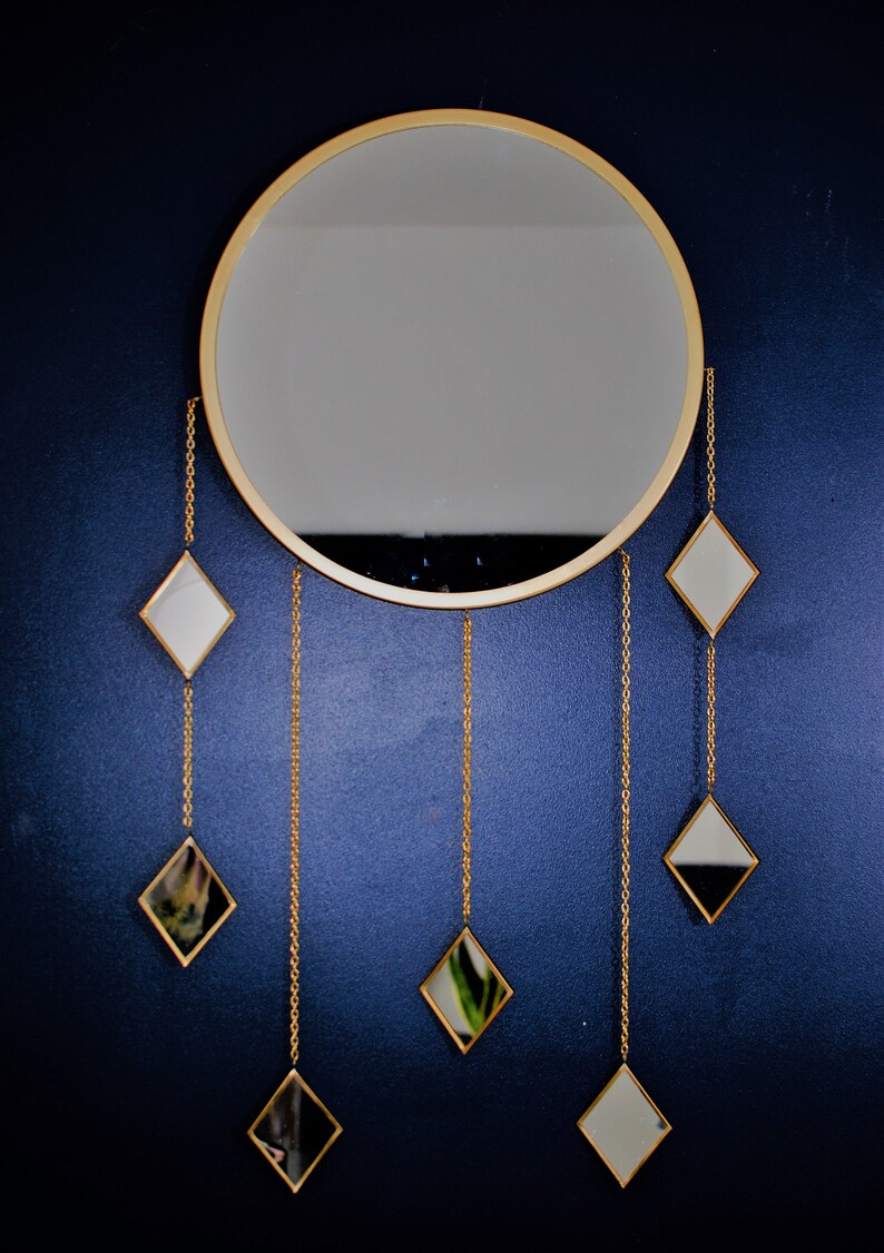 May include: A gold round mirror with a gold frame and six smaller diamond-shaped mirrors hanging from chains.