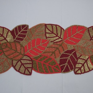 Könnte beinhalten: Ein geperlter Tischläufer mit einem Design aus mehreren Blättern in Gold-, Burgunder-, Korallen- und Pfirsichtönen.