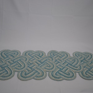 May include: A blue and white beaded table runner with a knotted design. The runner is made of small, round beads that are woven together to create an intricate pattern.