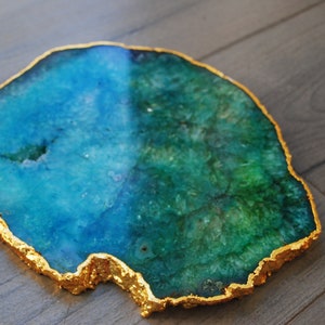 Puede incluir: Una rodaja de &aacute;gata decorativa con borde chapado en oro. La piedra natural presenta una mezcla de tonos azules y verdes. Esta pieza &uacute;nica se puede utilizar como posavasos o acento decorativo.