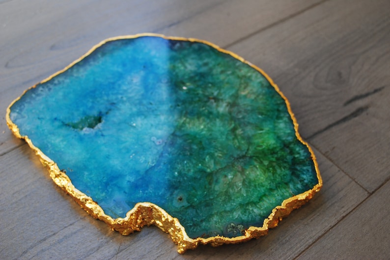 Puede incluir: Una rodaja de &aacute;gata decorativa con borde chapado en oro. La piedra natural presenta una mezcla de tonos azules y verdes. Esta pieza &uacute;nica se puede utilizar como posavasos o acento decorativo.