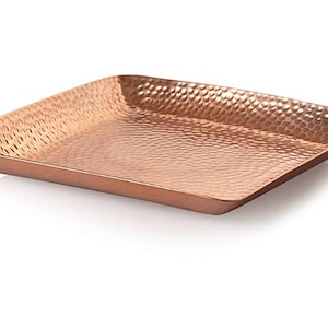 Może przedstawiać: Kwadratowa miedziana taca z młotkowanym wykończeniem. Taca wykonana jest z metalu i ma błyszczące, metaliczne wykończenie.