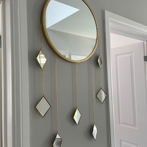 May include: A gold round mirror with a decorative chain hanging from the bottom with small diamond-shaped mirrors attached to the chain.