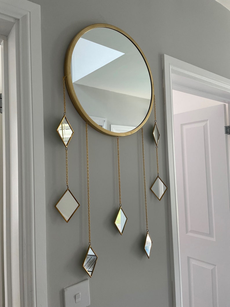 May include: A gold round mirror with a decorative chain hanging from the bottom with small diamond-shaped mirrors attached to the chain.