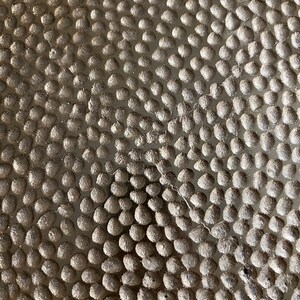 K&ouml;nnte beinhalten: Nahaufnahme einer strukturierten Oberfl&auml;che mit einem Muster aus kleinen, runden, erhabenen Punkten. Die Punkte sind in einem sich wiederholenden Muster angeordnet, wodurch ein subtiles, aber visuell interessantes Design entsteht.