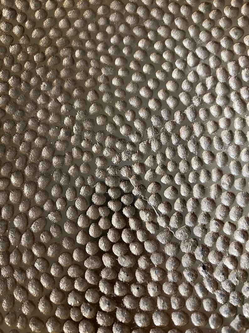 K&ouml;nnte beinhalten: Nahaufnahme einer strukturierten Oberfl&auml;che mit einem Muster aus kleinen, runden, erhabenen Punkten. Die Punkte sind in einem sich wiederholenden Muster angeordnet, wodurch ein subtiles, aber visuell interessantes Design entsteht.