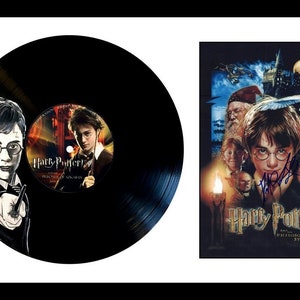 Puede incluir: Un disco de vinilo negro con una ilustración en blanco y negro de Harry Potter en la parte delantera. La etiqueta del disco presenta una foto de Harry Potter de la película "Harry Potter y la piedra filosofal" con el título de la película impreso en la etiqueta.