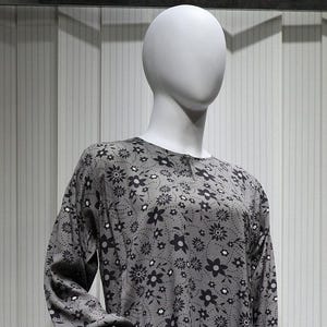 May include: A gray long-sleeved dress with a black floral print. The dress has a round neckline and long sleeves. The dress is on a white mannequin.