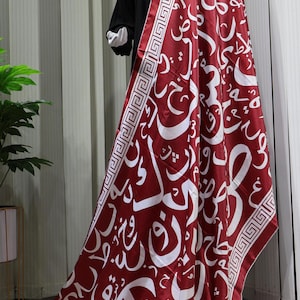 May include: A red satin scarf with a white Arabic calligraphy pattern and a white and red geometric border.