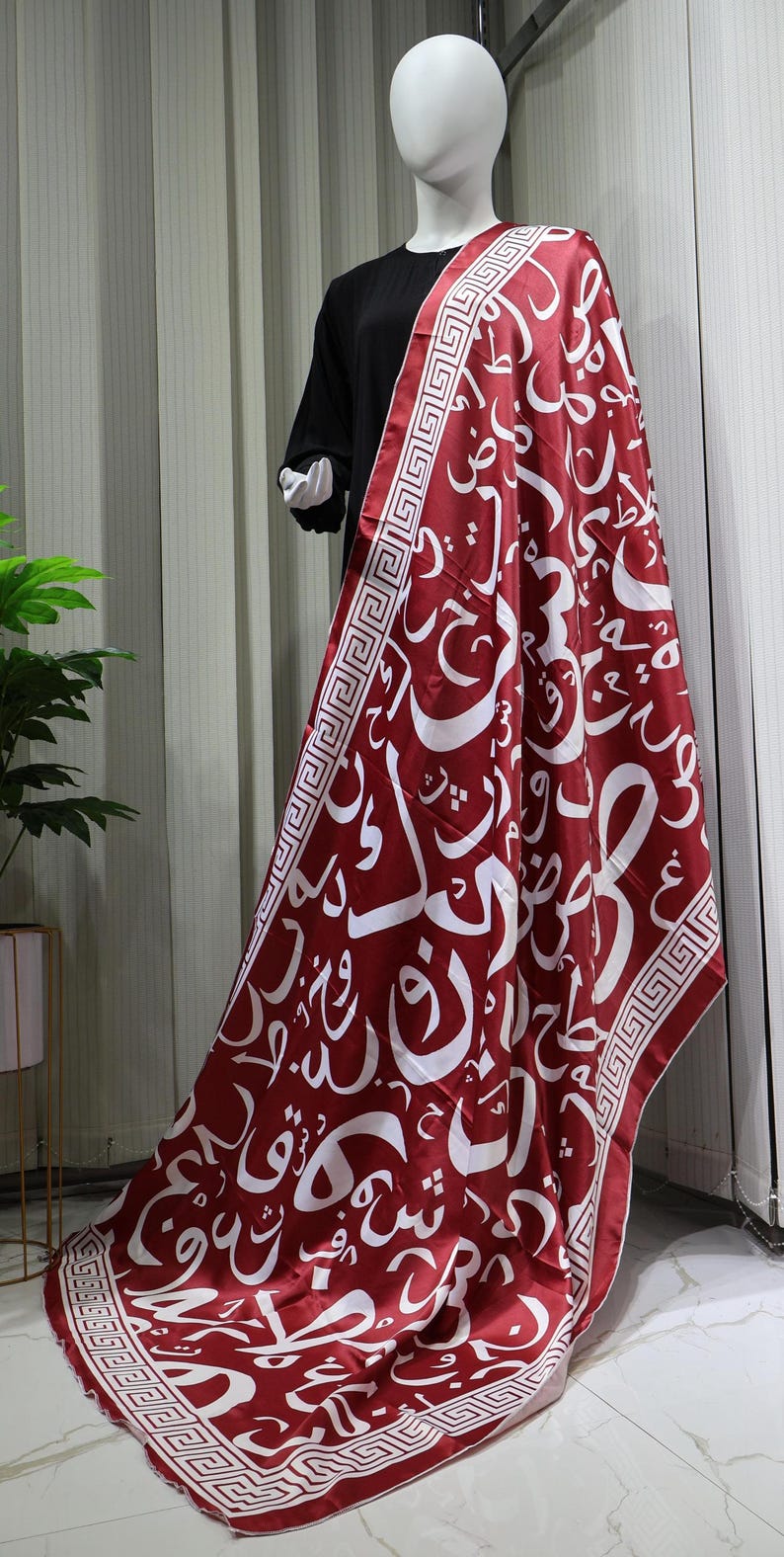 May include: A red satin scarf with a white Arabic calligraphy pattern and a white and red geometric border.