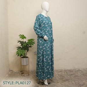 May include: A long-sleeved, floor-length dress in a teal blue color featuring a repeating pattern of small white flowers and green leaves. The garment is displayed on a white mannequin, showcasing a round neckline and a straight, flowing silhouette.