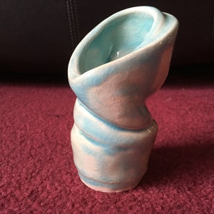 Puede incluir: Un pequeño jarrón de cerámica azul y blanco con un diseño único y retorcido. El jarrón está esmaltado y tiene una superficie texturizada.