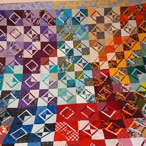May include: A colorful quilt made of various fabric squares with a diamond pattern. The quilt is made up of different colors, including purple, blue, green, red, orange, and yellow.