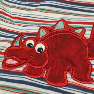 May include: Red and white striped baby onesie with a red embroidered dinosaur on the front. The dinosaur has a light blue crest and large eyes.