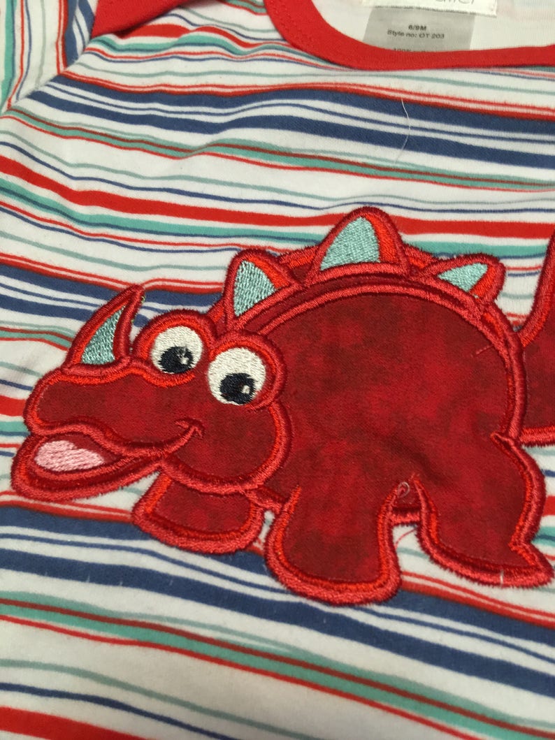 May include: Red and white striped baby onesie with a red embroidered dinosaur on the front. The dinosaur has a light blue crest and large eyes.