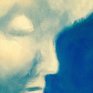 May include: A close-up of a painting depicting a face in profile, with the left side of the face painted in a light beige color and the right side of the face painted in a dark blue color.