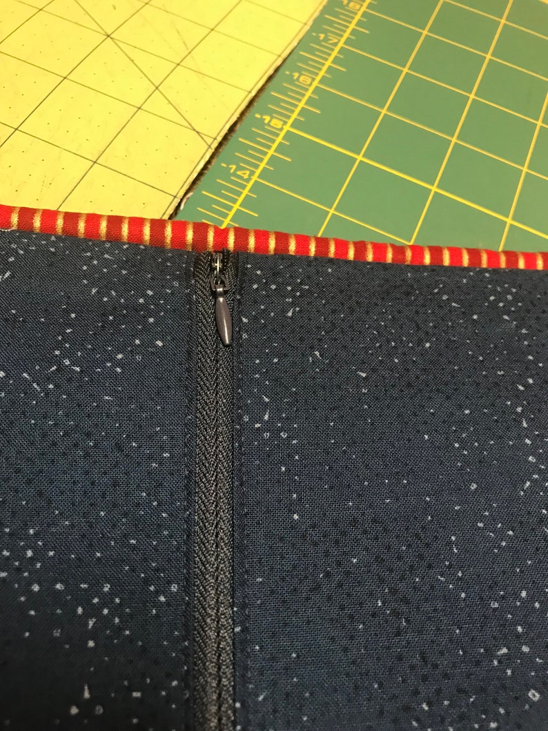 May include: A close-up of a black zipper sewn into a dark blue fabric with a white speckled pattern. The zipper has a silver pull tab.