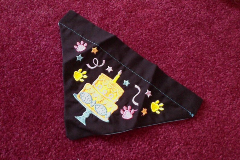 Pode incluir: Bandana de tecido preto para cachorro com um bolo de anivers&aacute;rio amarelo e branco, pegadas, estrelas e o n&uacute;mero "2" bordado.