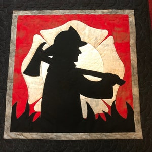 Może przedstawiać: Czarna sylwetka strażaka trzymającego siekierę przed czerwono-białym emblematem straży pożarnej.