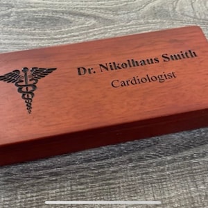 May include: A wooden box with a medical symbol and the text "Dr. Nikolhaus Smith Cardiologist" engraved on the top.