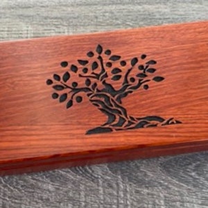 May include: A rectangular wooden box in reddish-brown. The lid is decorated with a black tree design, featuring a detailed canopy and trunk. The box's design incorporates a natural tree motif.