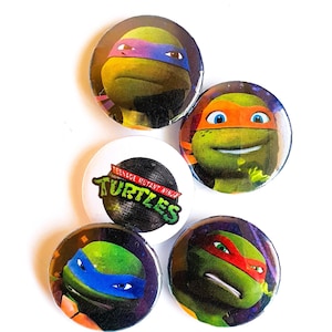 Puede incluir: Cinco botones de las Tortugas Ninja. Cada botón presenta una tortuga diferente con sus colores y armas distintivos. Un botón presenta el logotipo de las Tortugas Ninja.