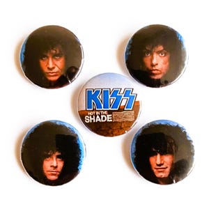 Puede incluir: Cuatro botones redondos con imágenes de la banda KISS. Un botón presenta el logotipo de la banda con el texto "KISS NOT IN THE SHADE". Los otros tres botones presentan miembros individuales de la banda.