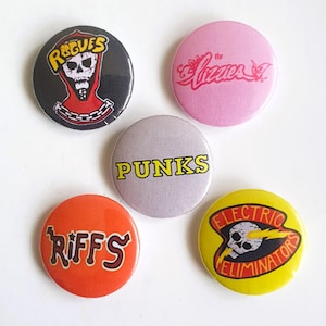 Puede incluir: Cinco botones redondos y coloridos con nombres de bandas y logotipos. Los botones presentan una calavera y huesos cruzados, una calavera con un rayo, las palabras "PUNKS", "RIFFS" y "The Lizzies".