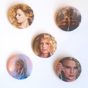 May include: Five round button pins featuring different images of a woman with blonde hair. The buttons are white with a silver border.
