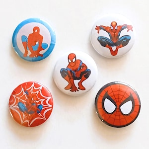 May include: Five circular badges showcasing Spider-Man designs. The badges feature the superhero in different poses, using red, blue, and white colours. One badge displays Spider-Man's mask with white eye shapes.