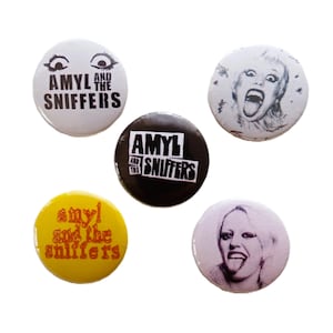以下が含まれることがあります： 5つの丸いピンバッジのコレクション。さまざまな色とフォントで「AMYL AND THE SNIFFERS」というテキストが書かれています。一部のバッジには、舌を出している女性のイラストが描かれています。