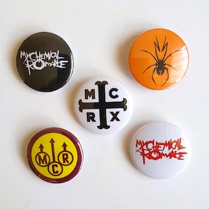 May include: Five round black and white buttons with different My Chemical Romance logos. The logos include the band's name, a spider, a cross with "MCRX" on it, and a symbol with "MCR" in a circle.