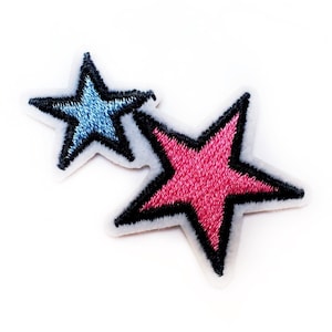 May include: Two embroidered stars, one blue and one pink, with black outlines. The stars are on a white background.