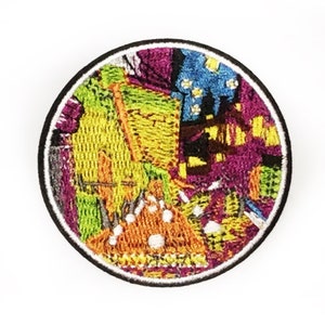 May include: A round embroidered patch with a colorful abstract design. The patch features a black border with a white stitch detail. The design includes yellow, purple, blue, and orange thread, creating a textured appearance.