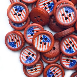 Könnte beinhalten: Eine Ansammlung runder Holzknöpfe mit patriotischem Design. Jeder Knopf zeigt ein rot-weiß-blaues amerikanisches Flaggenmotiv. Die Knöpfe haben einen Durchmesser von etwa 2,5 cm und vier Löcher zum Annähen.